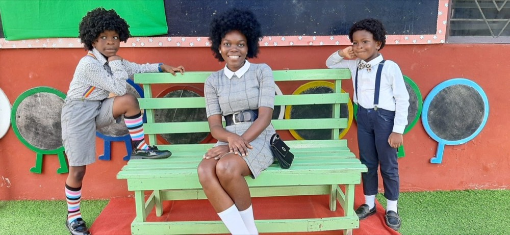 Two pupils dressed up either side of a teacher seated on a green bench