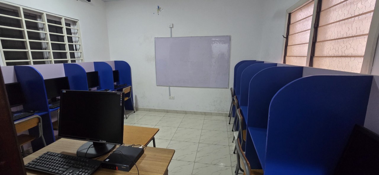 The school computer room, with monitors and keyboards in blue study carrels facing a whiteboard